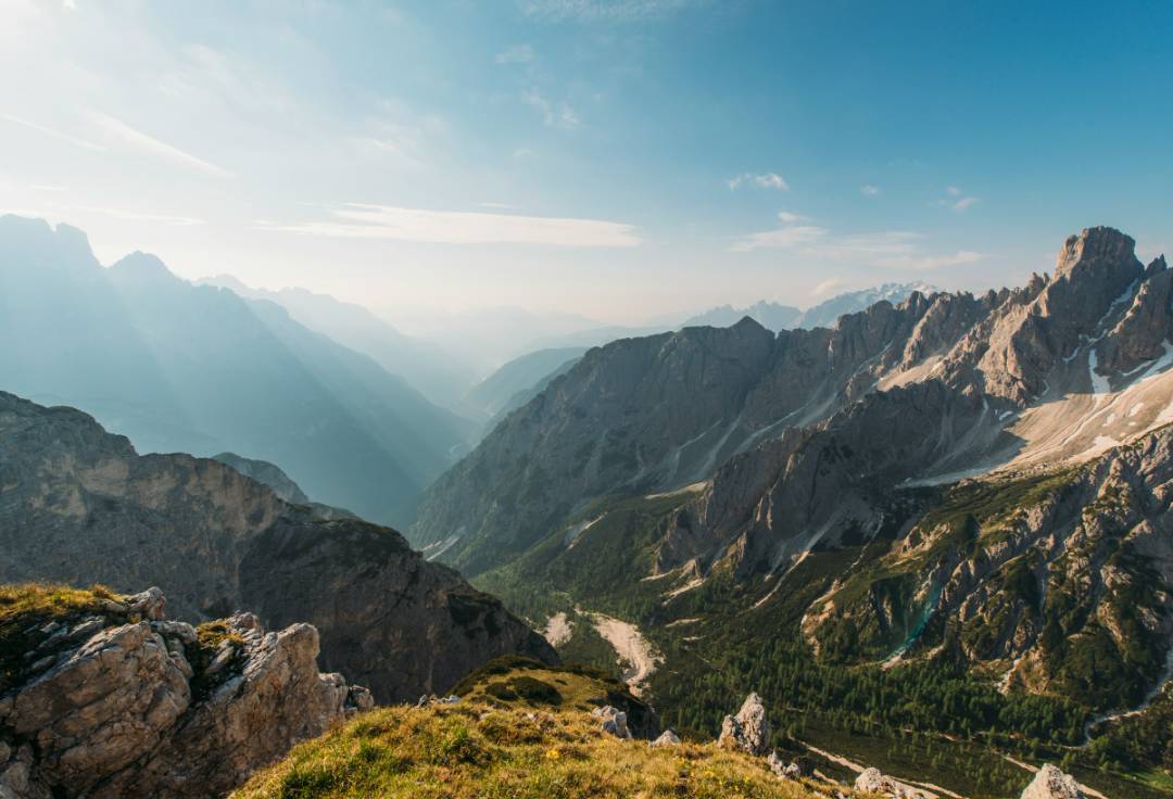 Panoramic view from a mountain summit, showcasing rugged peaks and lush valleys under a clear blue sky.