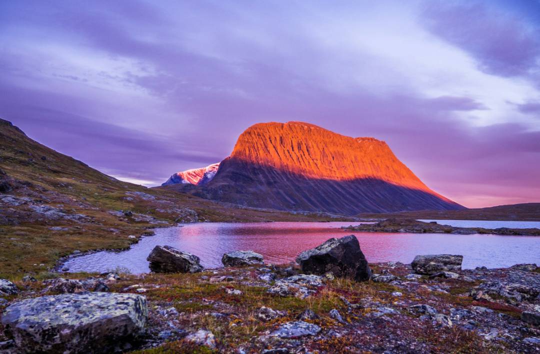 The sun sets behind a mountain, casting warm hues over the rugged landscape.