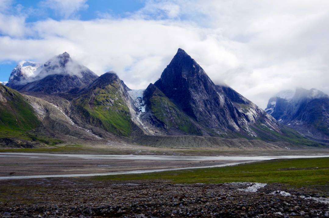 Snow-capped mountains in Auyuittuq National Park, showcasing Mount Thor's dramatic vertical face and surrounding glaciers.