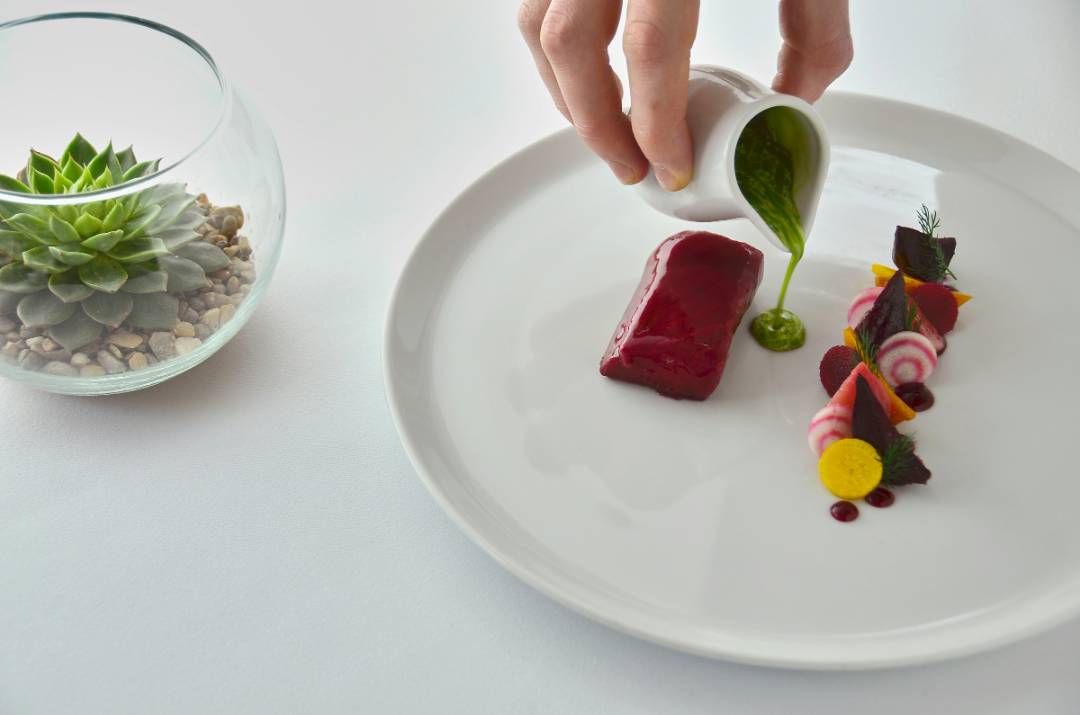 Chef che impiatta una raffinata preparazione con barbabietola, verdure e salsa verde in un ristorante stellato Michelin di Milano